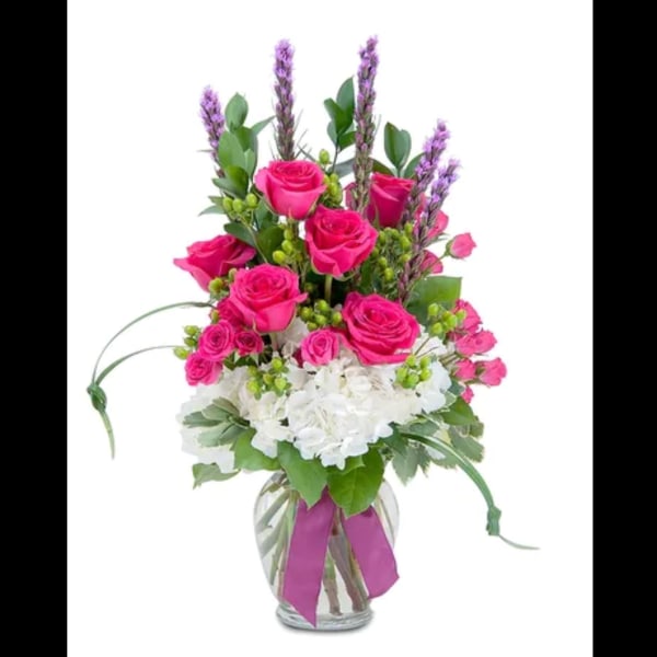 Pink roses and white flowers in a glass vase with a purple ribbon