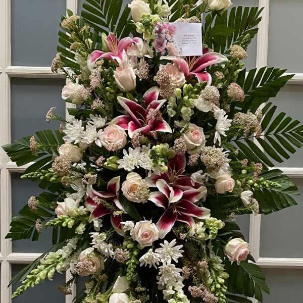 Large standing floral spray with pink lilies, white roses, and greenery on an easel