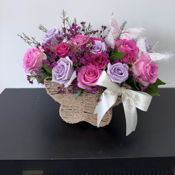 Pink and lavender roses in a woven basket with a ribbon bow