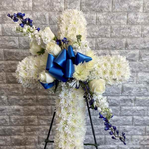 White floral standing spray with blue ribbon and purple accents on an easel