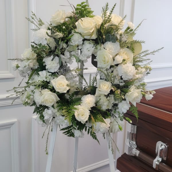 White rose and hydrangea funeral wreath on a stand beside a casket