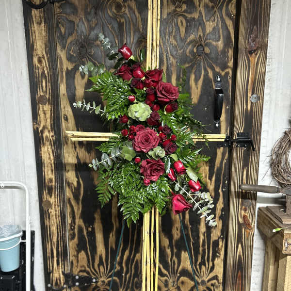 Tall cross-shaped standing spray with red roses and greenery on a wooden easel.