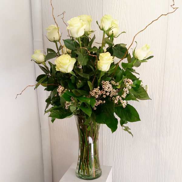 White roses in a clear glass vase with small white filler flowers