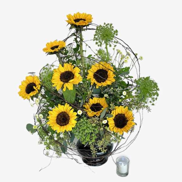 Sunflower arrangement in a black vase with a small candle beside it