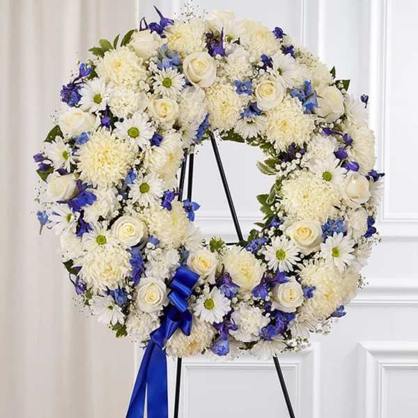 White and blue floral wreath on a stand with a blue ribbon