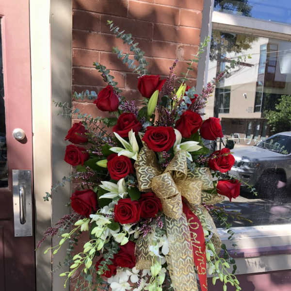 Tall standing arrangement of red roses and white lilies with a gold ribbon