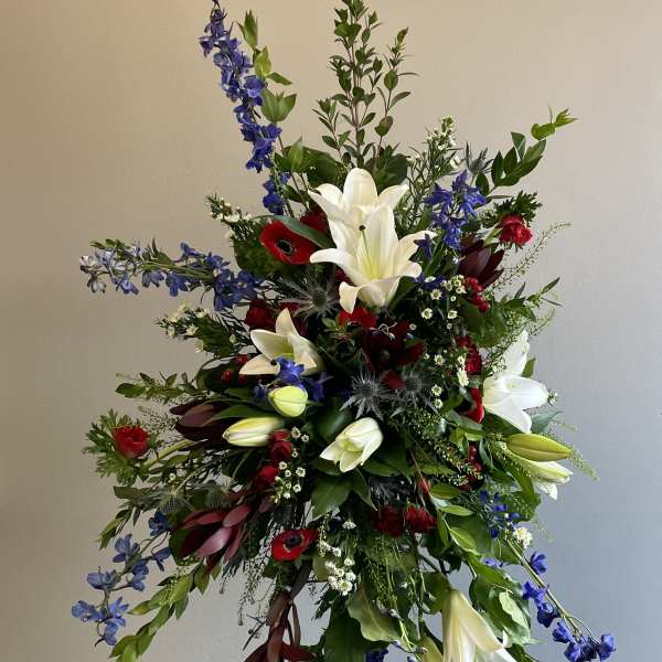 Tall floral spray with white lilies, red blooms, and blue flowers on a stand