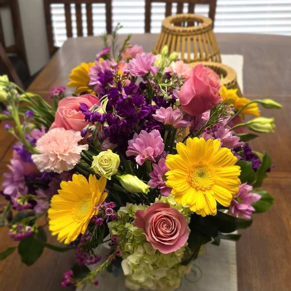 Mixed bouquet of pink, yellow, and purple flowers in a glass vase