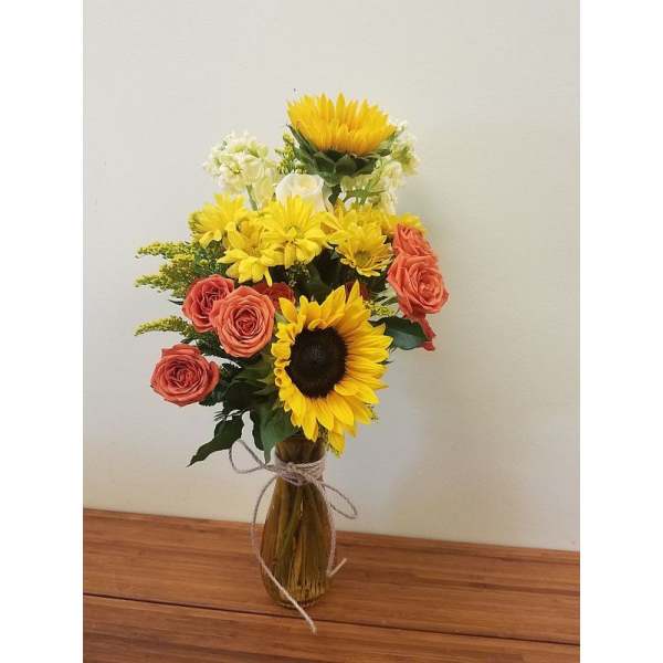 Bouquet of sunflowers, coral roses, and white flowers in a glass vase
