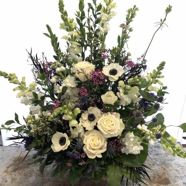 Tall floral arrangement with cream roses, white anemones, and pale snapdragons