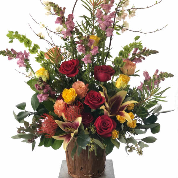 Tall mixed flower arrangement in a wooden container with red and yellow roses