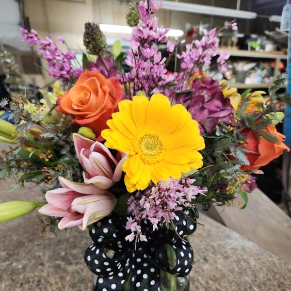 Mixed bouquet in a glass vase with a black polka-dot ribbon