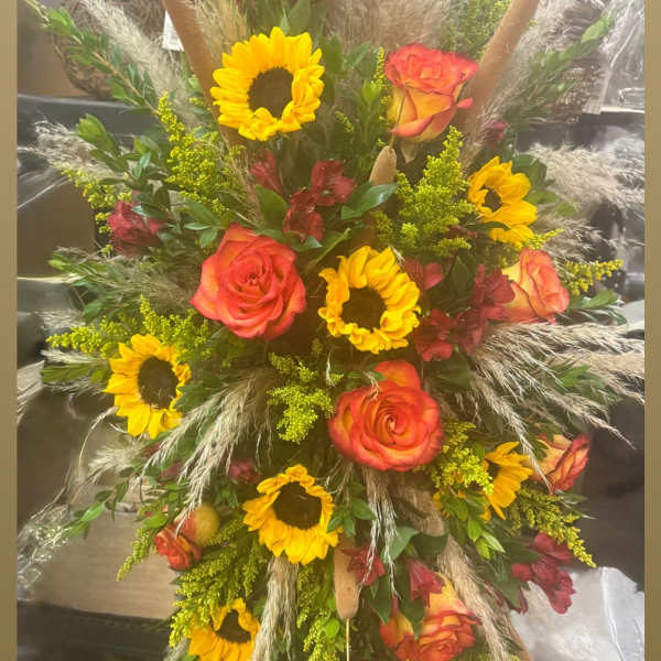Tall arrangement of orange roses and sunflowers with dried grasses