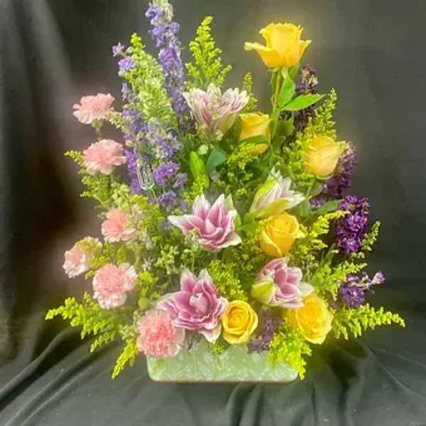 Mixed bouquet with yellow roses, pink carnations, and purple flowers in a green container