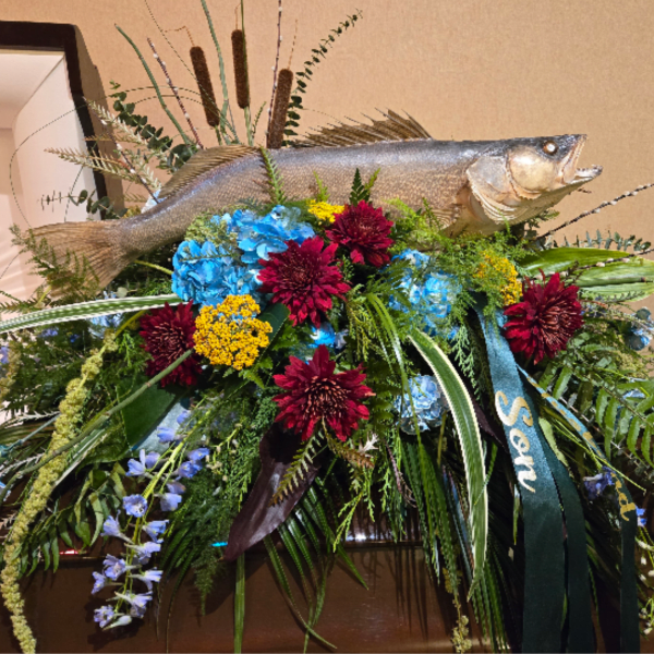 Fishing-themed casket spray with blue and red flowers, cascading ferns, and a mounted fish on top