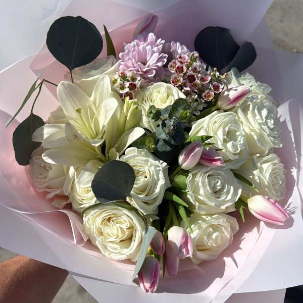 Bouquet of white roses, lilies, and pink tulips wrapped in pale paper