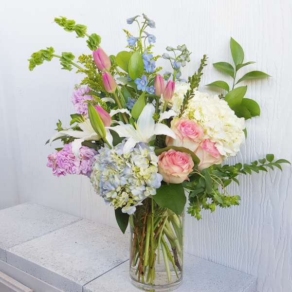 Mixed bouquet of pink roses, white lilies, and hydrangeas in a glass vase