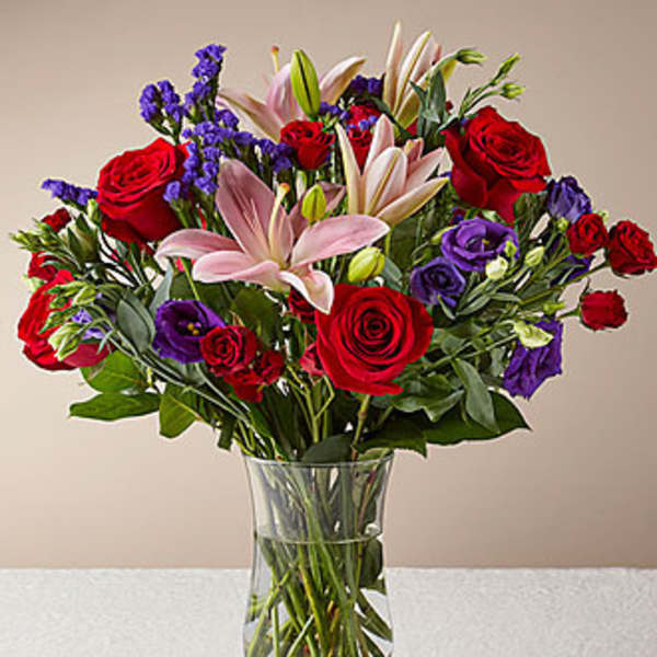 Bouquet of red roses, pink lilies, and purple flowers in a glass vase