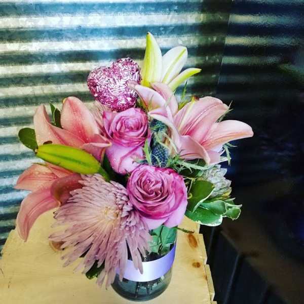 Pink lilies and roses arranged in a glass vase with a glittery heart pick.