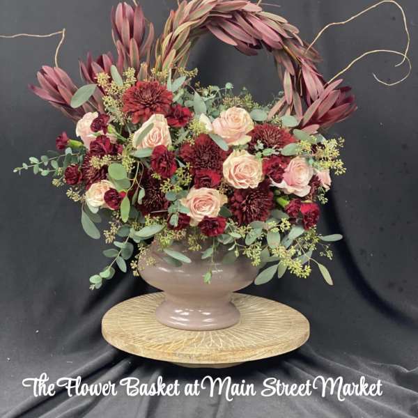 A burgundy and blush floral arrangement in a pedestal vase with a decorative arch.