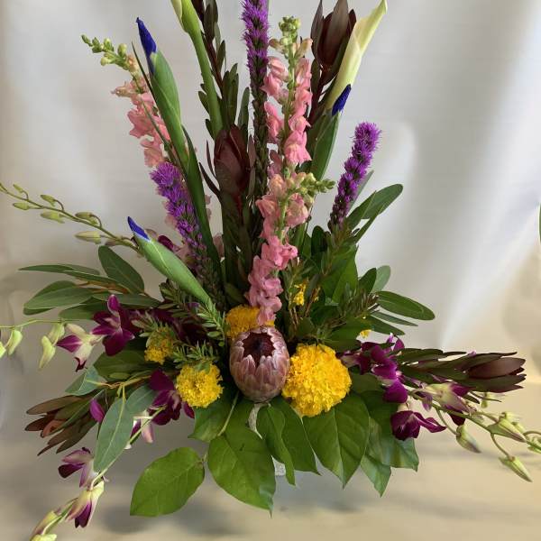 Tall mixed floral arrangement with calla lilies, orchids, and purple spikes