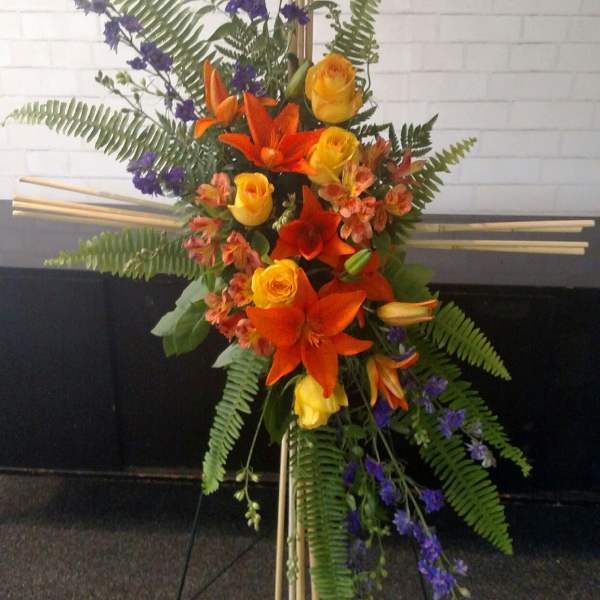 Tall floral standing arrangement with orange lilies, yellow roses, and purple flowers