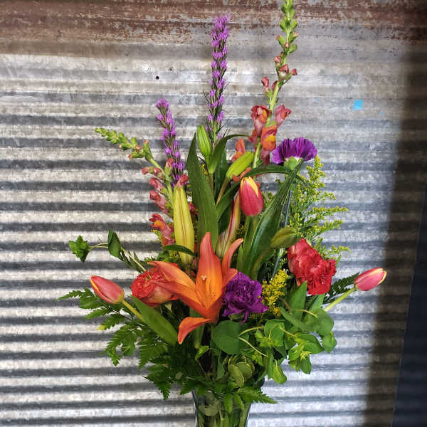 Tall mixed bouquet in a clear glass vase with lilies, tulips, and purple spikes