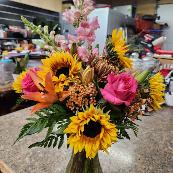 Mixed bouquet with sunflowers, pink roses, lilies, and snapdragons in a glass vase