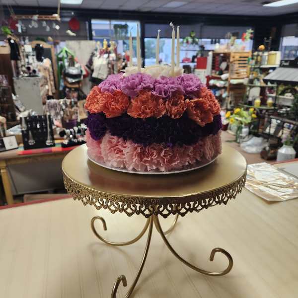 Round floral cake with pink, purple, and orange carnations and white candles
