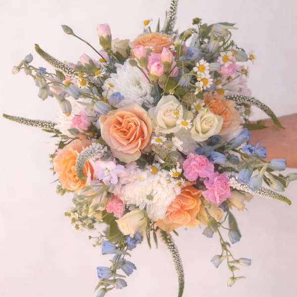 Hand-tied bouquet of peach roses, white mums, and pastel pink and blue flowers.
