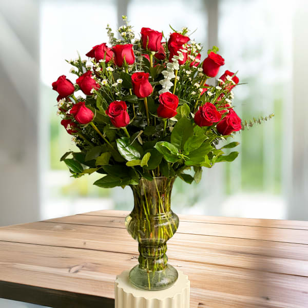 Red roses arranged in a clear glass vase with small white filler flowers.