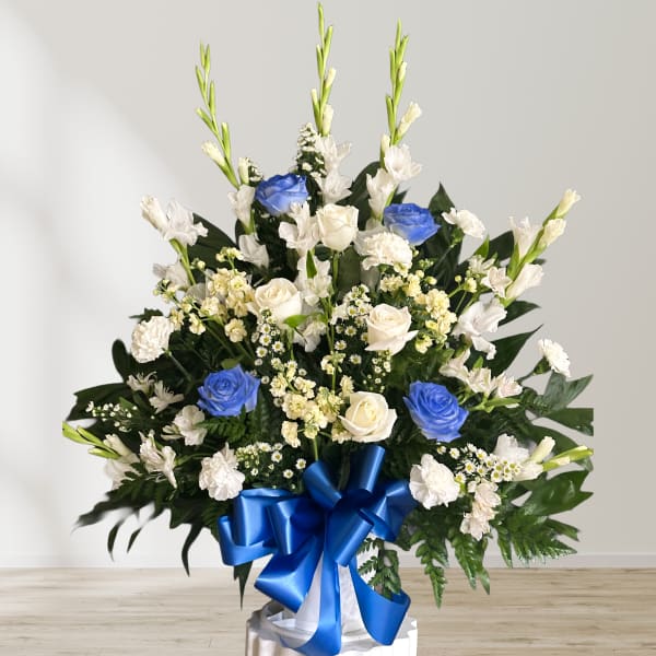 Large white and blue floral arrangement with a blue ribbon on a pedestal