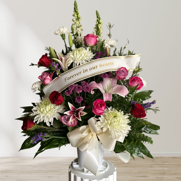 Standing sympathy spray with pink and white flowers and a memorial ribbon
