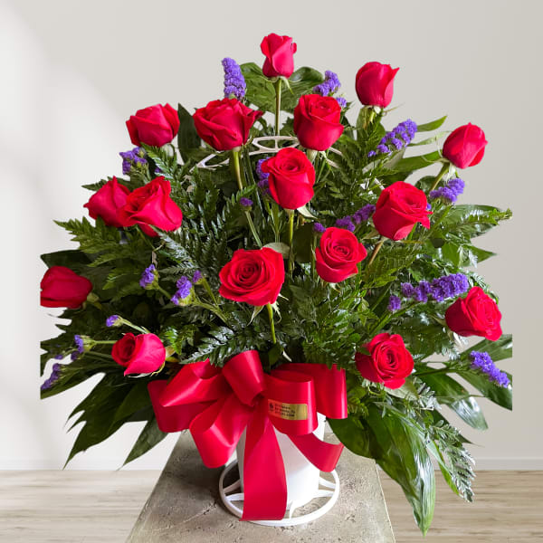 Red roses arranged in a white vase with a large red ribbon