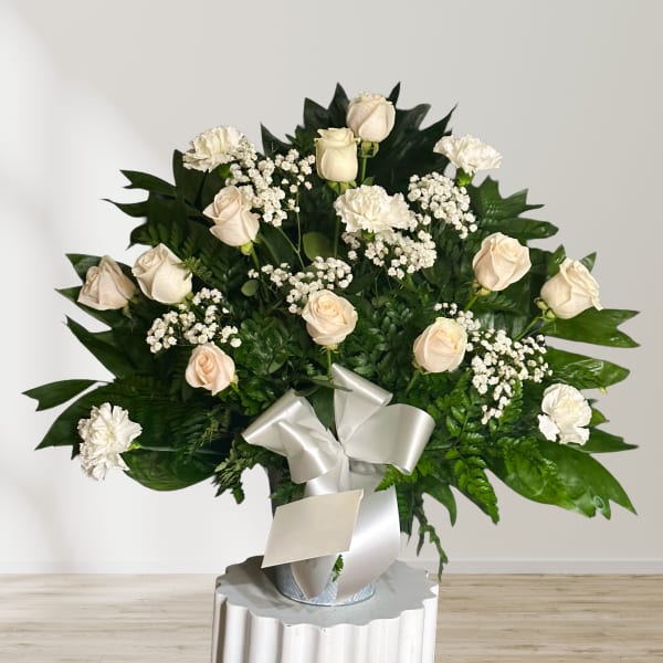 Cream roses and white carnations in a silver vase with a white ribbon