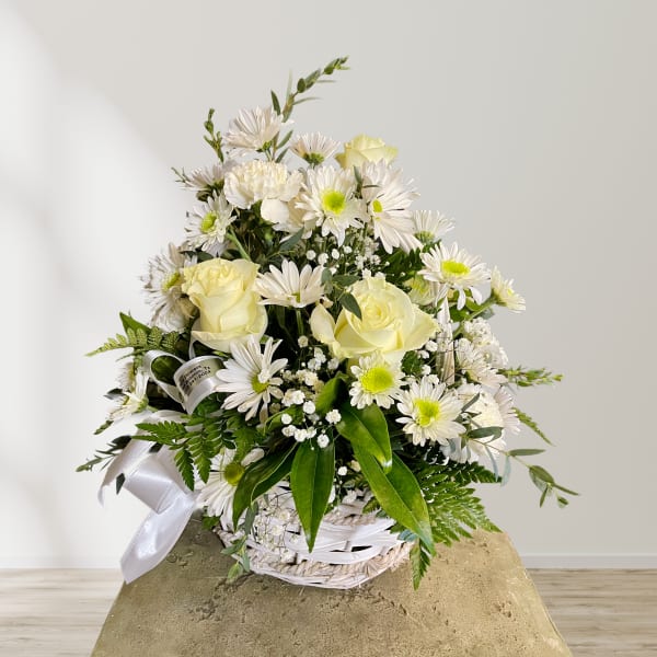White roses and daisies arranged in a white basket with a silver ribbon