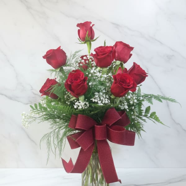 Red roses arranged in a glass vase with a burgundy ribbon