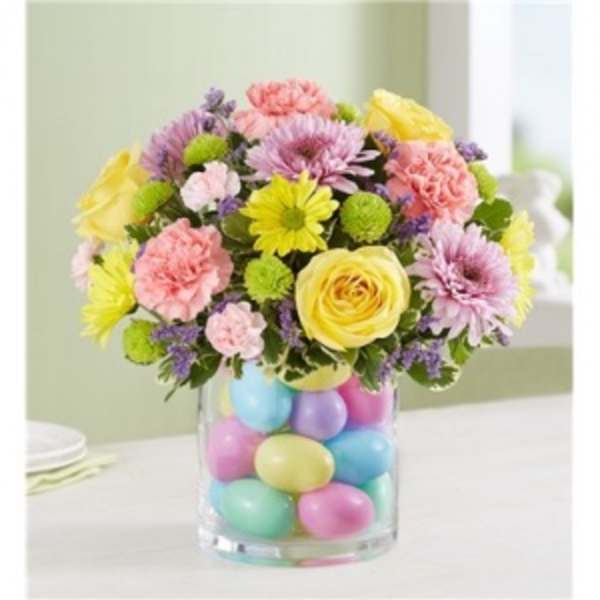 Pastel mixed flower arrangement in a clear vase filled with colorful eggs.