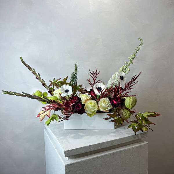 Long floral arrangement with white and burgundy roses in a white rectangular vase