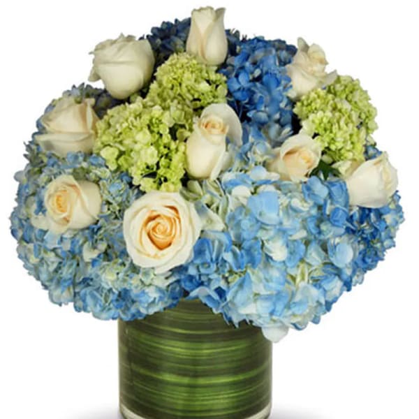 Blue hydrangeas and white roses arranged in a green glass vase