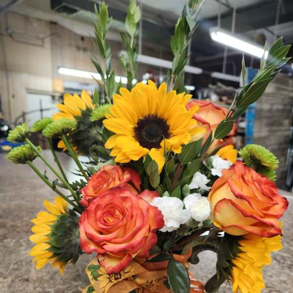 Sunflowers and orange roses arranged in a pumpkin-shaped vase