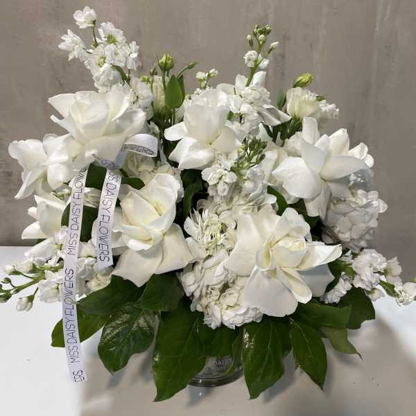 White floral arrangement in a glass vase with ribbon streamers