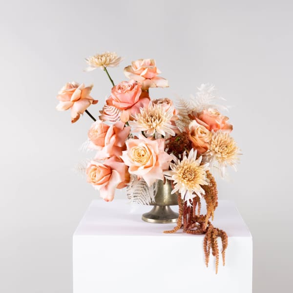 Peach roses and cream blooms arranged in a gold vase