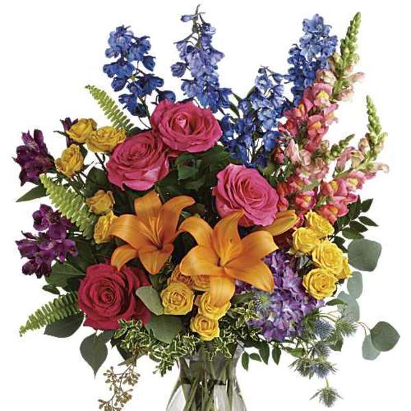 Tall mixed bouquet of pink roses, orange lilies, and bright assorted blooms in a clear glass vase.