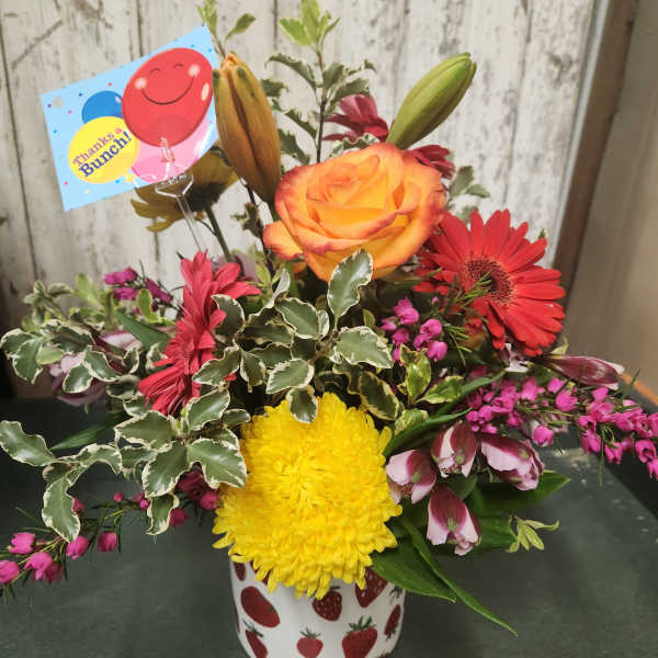 Mixed flower arrangement in a strawberry-patterned mug with a thank-you card