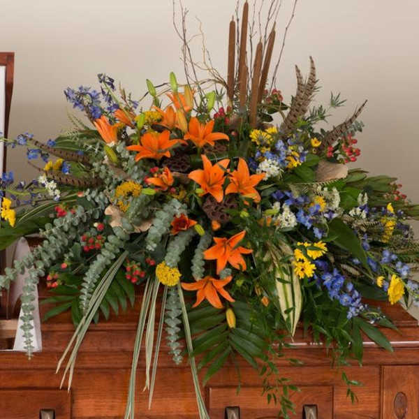 Large floral spray with orange lilies and mixed flowers on a casket