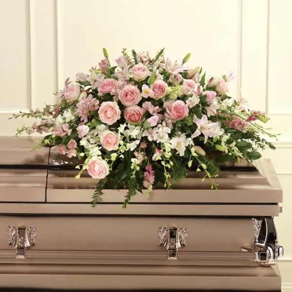 Pink and white floral casket spray on a beige casket