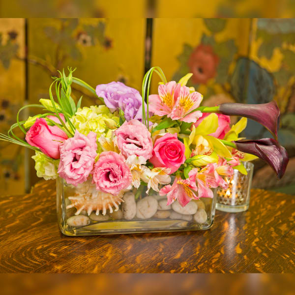 Mixed pink and yellow flowers in a rectangular glass vase with stones
