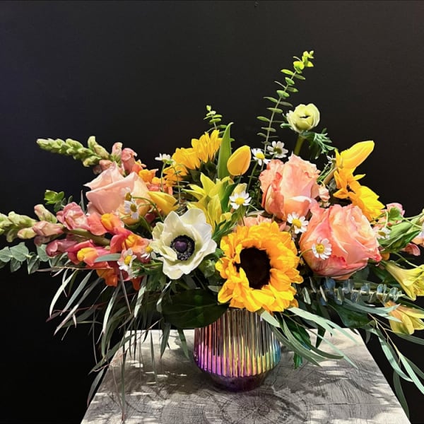 Mixed bouquet of roses, sunflowers, tulips, and snapdragons in a rainbow glass vase