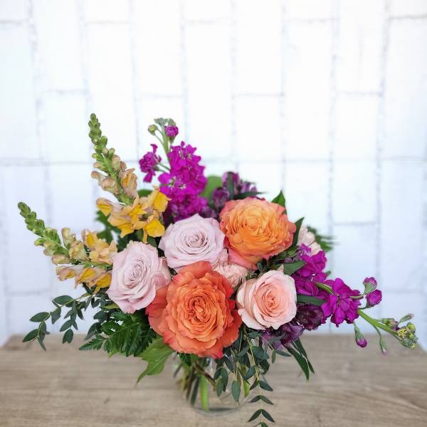 Bouquet of peach and blush roses with purple flowers in a glass vase